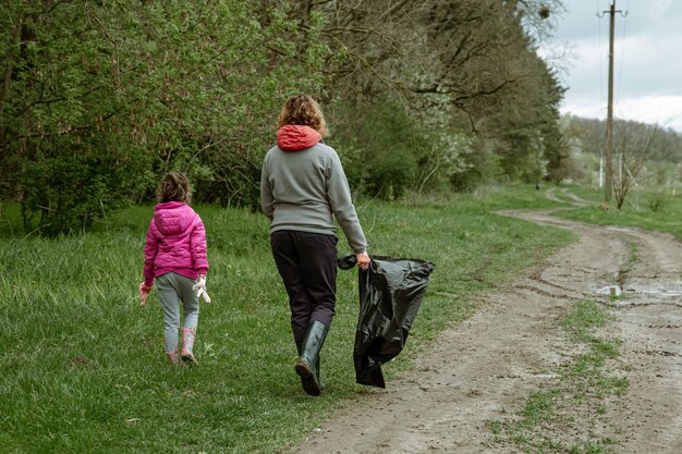 Mama i córka z workami na śmieci oczyszczają środowisko ze śmieci.