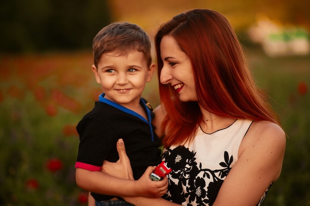 Bezpłatne zdjęcie mama posiada uroczy mały syn stojący na zielonym polu z makami