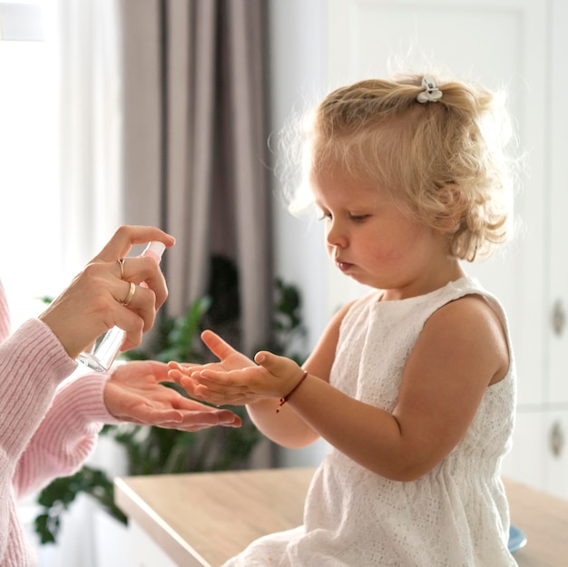 Mama rozpyla w domu środek dezynfekujący do rąk dziecka