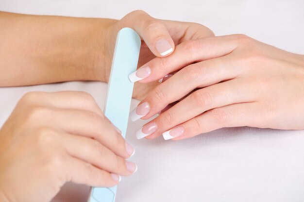 Manikiurzystka poleruje kobiece paznokcie francuskim manicure