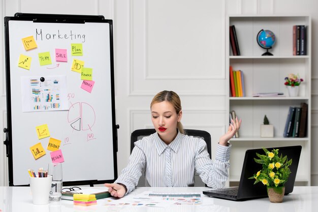 Marketing młoda śliczna biznesowa dama w pasiastej koszuli w biurze, patrząc na notatki obok biurka