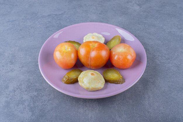 Marynowane warzywa na fioletowym talerzu. Czerwony pomidor z plastrami ogórka i zielonym patty z patelni.