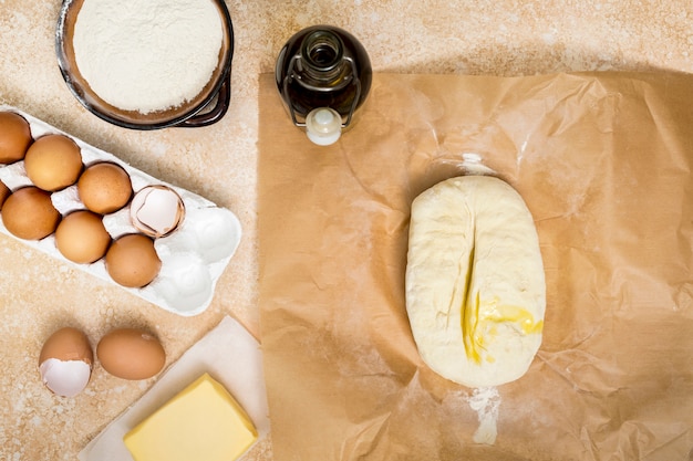 Masło; jajko w pudełku kartonowym; mąka i ugniatane ciasto i olej na blacie kuchennym