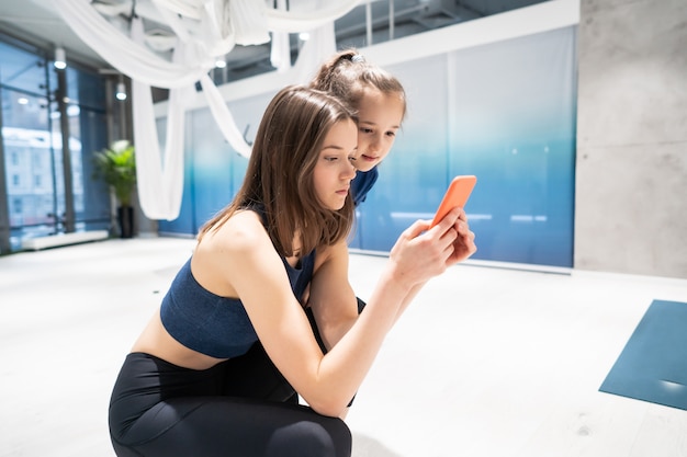 Matka i dziewczyna używa telefon w gym dla oglądać wideo