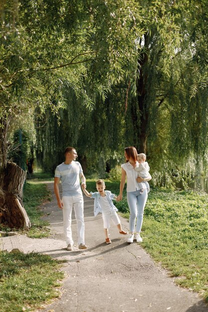 Matka, ojciec, starszy syn i córeczka spacerują po parku. Rodzina ubrana w biało-jasnoniebieskie ubrania