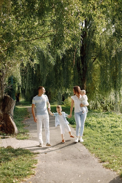 Matka, ojciec, starszy syn i córeczka spacerują po parku. Rodzina ubrana w biało-jasnoniebieskie ubrania