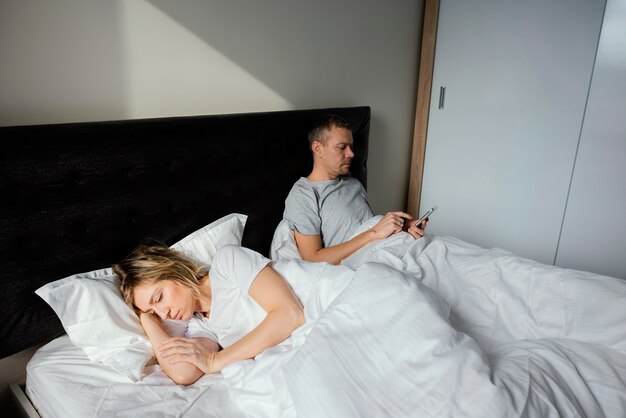Mąż korzysta z telefonu komórkowego, gdy żona śpi