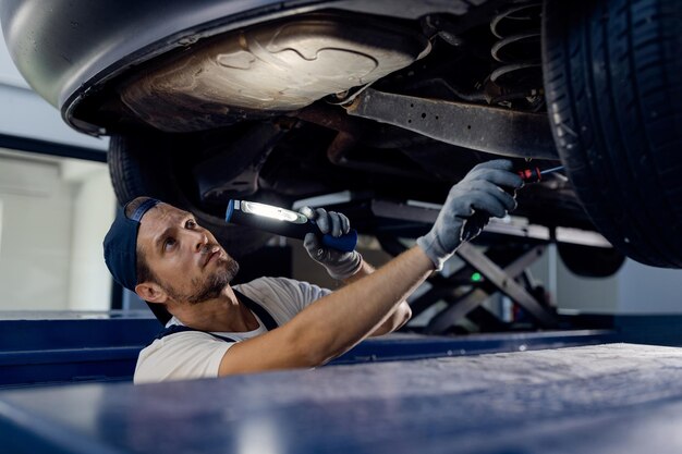 Mechanik samochodowy badający podwozie samochodu z latarką w warsztacie