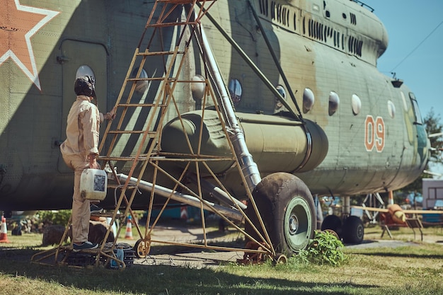 Mechanik w mundurze i hełmie latającym zajmuje się konserwacją dużego śmigłowca wojskowego w skansenie.