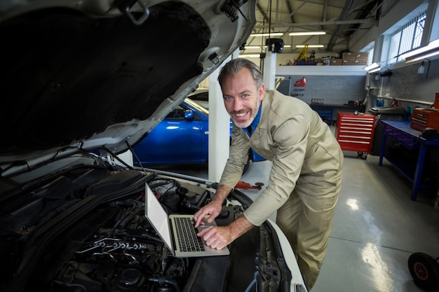 Mechanik za pomocą laptopa podczas serwisowania silnika samochodu