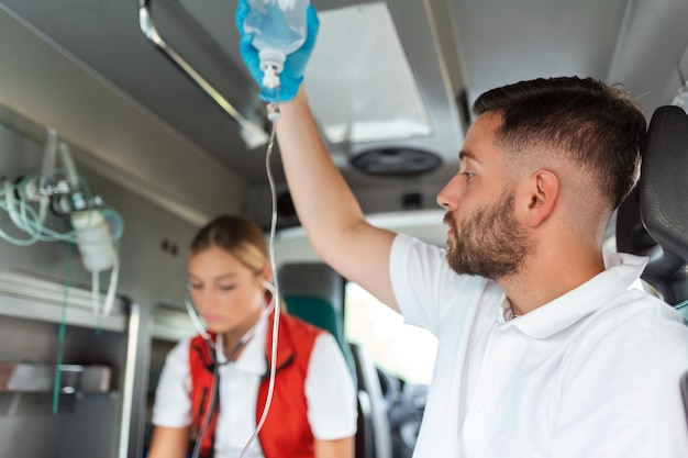 Medycy z rannym pacjentem podający infuzję Młodzi sanitariusze płci męskiej trzymający roztwór dożylny Lekarka słuchająca serca pacjenta