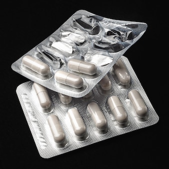Medycyna zbliżenie białych tabletek kapsułek w dwóch pełnych i otwartych blistrach na czarnym tle