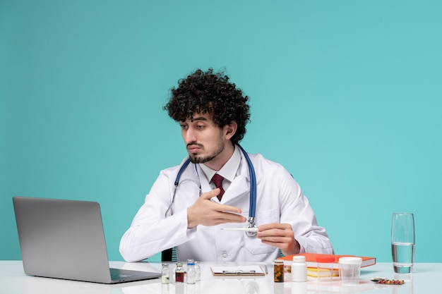 Medyczny poważny ładny przystojny lekarz pracuje na komputerze w fartuchu pokazując leki