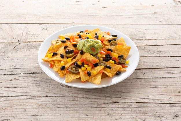 Meksykańskie chipsy tortilla nachos z czarną fasolą, guacamole, pomidorem i jalapeno na drewnianym stole