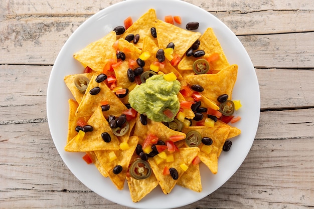 Meksykańskie chipsy tortilla nachos z czarną fasolą, guacamole, pomidorem i jalapeno na drewnianym stole