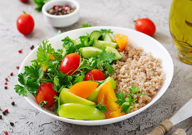 Menu dietetyczne. Zdrowa sałatka wegetariańska świeżych warzyw - pomidorów, ogórków, słodkiej papryki i owsianki na misce. Wegańskie jedzenie.