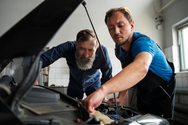 Bezpłatne zdjęcie męscy mechanicy pracujący razem nad samochodem w sklepie