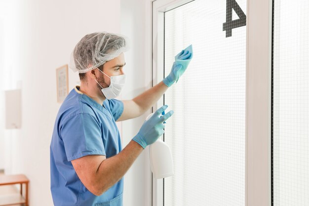 Męska pielęgniarka dezynfekuje okno przy szpitalem