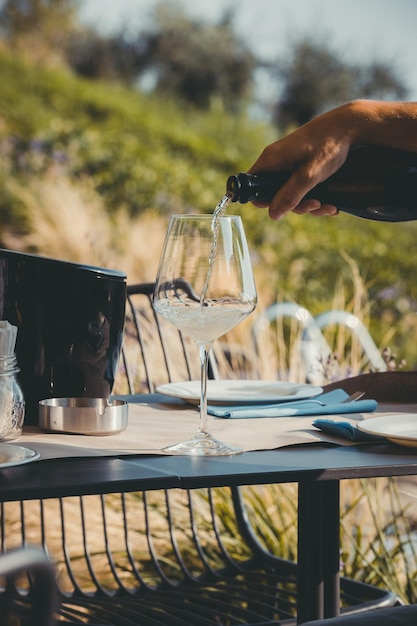 Męska ręka nalewająca napój alkoholowy w eleganckim kieliszku na stole podczas imprezy plenerowej