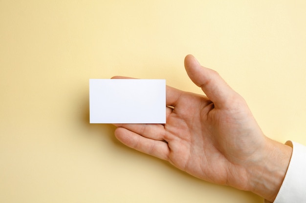 Męska ręka trzyma pustą wizytówkę na miękkiej żółtej ścianie dla tekstu lub projektu. Puste szablony kart kredytowych do kontaktu lub wykorzystania w biznesie. Biuro Finansów. Copyspace.