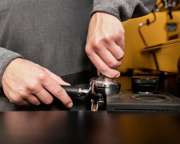 Męski barista w fartuchu za pomocą profesjonalnego kubka do ekspresu do kawy