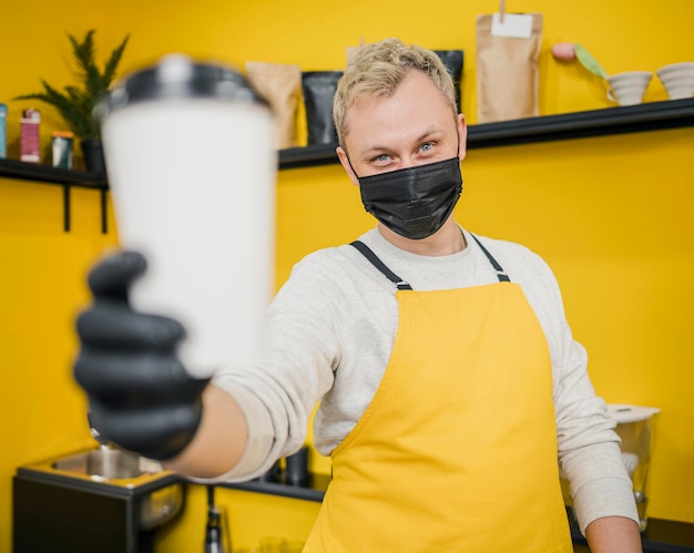 Męski barista z medyczną maską trzyma filiżankę