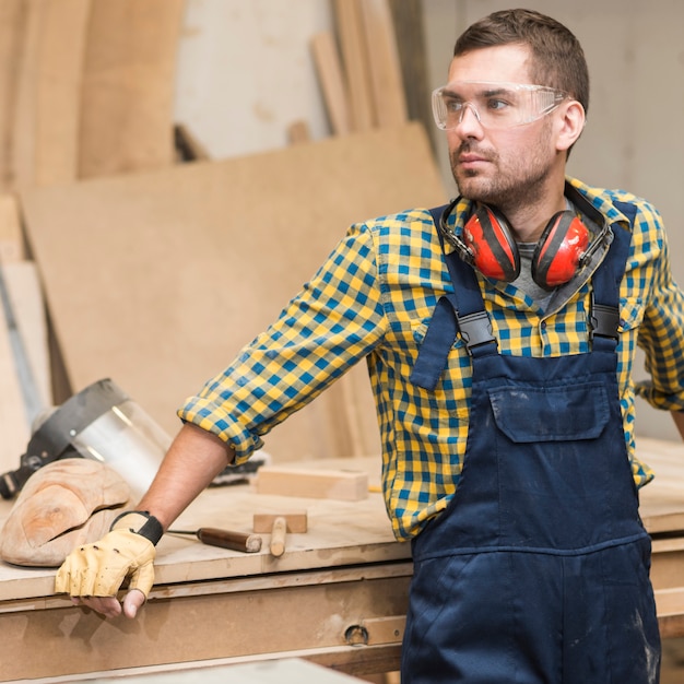 Bezpłatne zdjęcie męski cieśla stoi przed workbench patrzeje daleko od