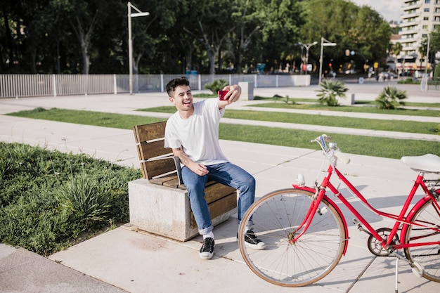 Męski cyklisty obsiadanie na ławce bierze selfie na telefonie komórkowym