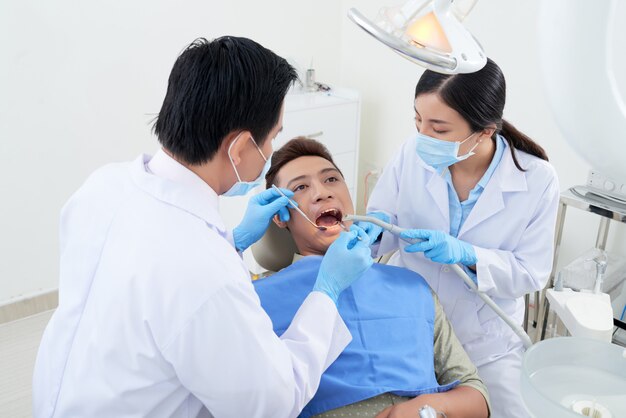Męski dentysta i pielęgniarka egzamininuje Azjatyckich pacjentów zęby przy kliniką