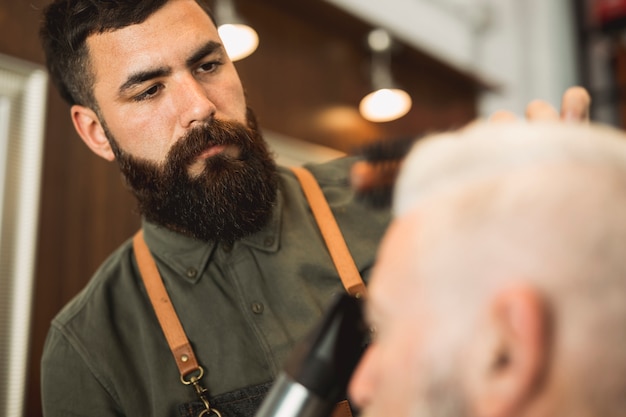 Męski fryzjer z suszarką do włosów współpracuje z klientem starszym
