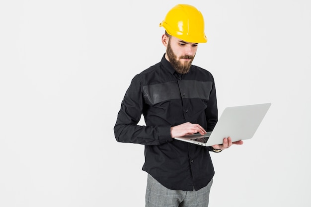 Męski inżynier jest ubranym hardhat używać laptop przeciw białemu tłu