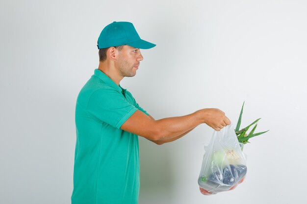 Męski kurier dostarczający woreczki polietylenowe z warzywami w zielonej koszulce z daszkiem