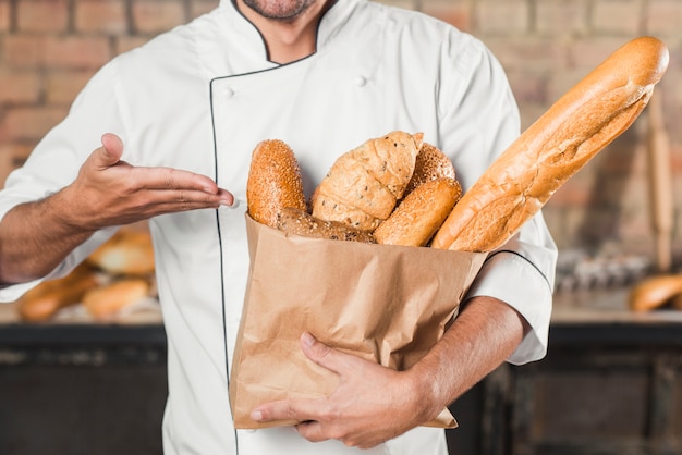 Męski piekarniany pokazuje bochenek chleby w brown papierowej torbie