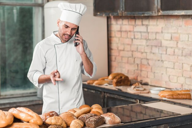 Męski piekarz opowiada na telefon komórkowy pozyci w piekarni gestykulować