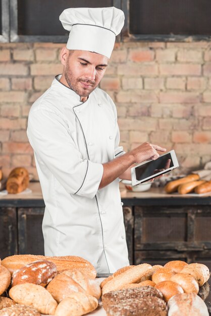 Męski piekarz patrzeje asortyment chleby używa cyfrową pastylkę