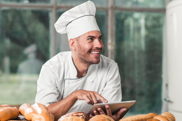 Męski piekarz używa cyfrową pastylkę z piec chlebami