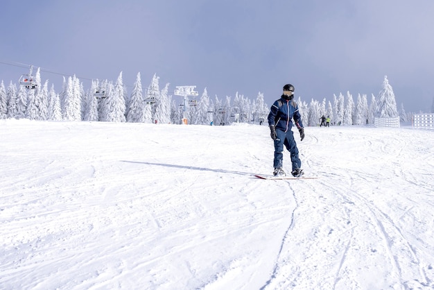 Męski snowboardzista zjeżdżający ze stoku z pięknym zimowym krajobrazem w tle