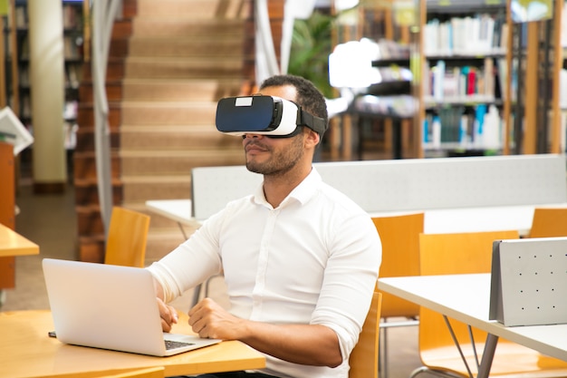 Męski uczeń używa VR słuchawki podczas pracy w bibliotece