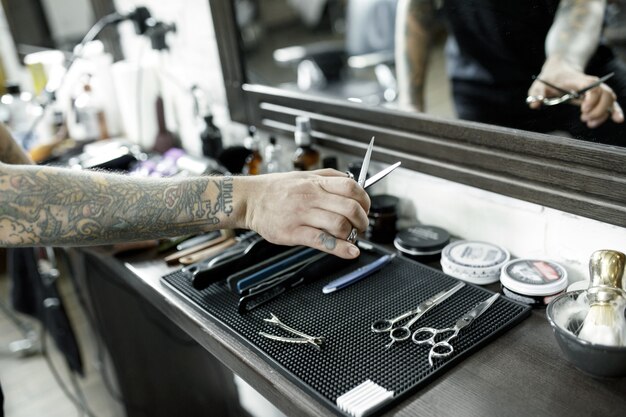 Męskie dłonie i narzędzia do strzyżenia brody w zakładzie fryzjerskim. Vintage narzędzia fryzjera. Ręka mistrza ma tatuaż z napisem golenie