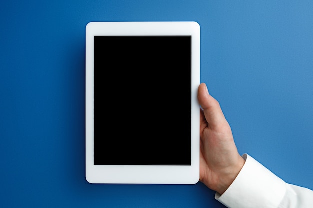 Męskiej ręki trzymającej tablet z pustym ekranem na niebiesko