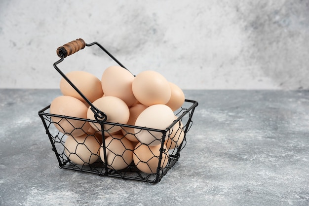 Bezpłatne zdjęcie metalowy kosz świeżych organicznych surowych jaj na marmurowej powierzchni.
