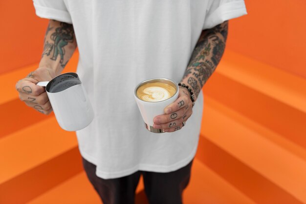 Mężczyzna barista z tatuażami dodający mleka do kawy