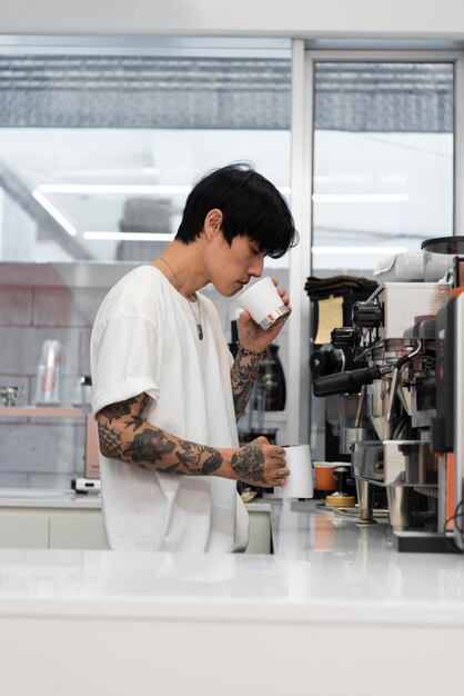 Mężczyzna barista z tatuażami pachnący świeżo mieloną kawą w filiżance