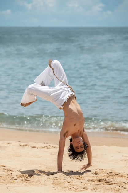 Mężczyzna bez koszuli ćwiczący capoeira samotnie na plaży