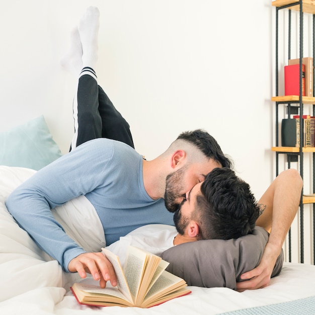 Mężczyzna całuje swojego chłopaka leżącego na łóżku z le opierając się na ścianie