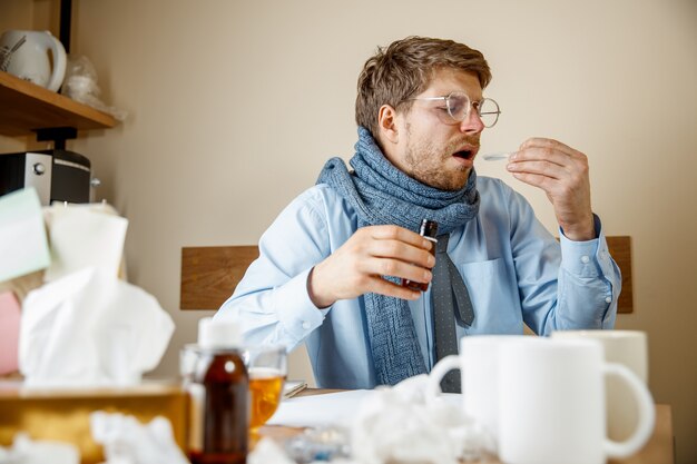 Mężczyzna czuje się chory i zmęczony. mężczyzna z kubkiem pracuje w domu, biznesmen przeziębiony, grypa sezonowa.