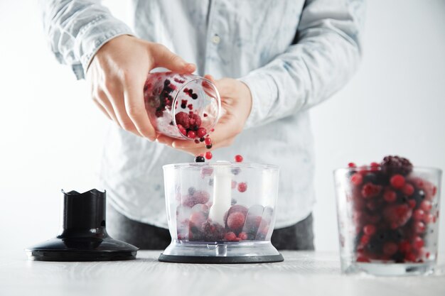 Mężczyzna dodaje mrożone jagody do skoncentrowanego blendera, a następnie przygotowuje smaczny napój smoothie, który odświeży latem. Nieostre szkło z mrożonymi jagodami z przodu w pobliżu