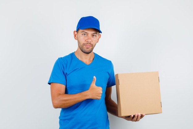 Mężczyzna dostawy, trzymając karton z kciukiem w niebieską koszulkę