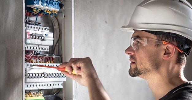Mężczyzna, elektryk pracujący w tablicy rozdzielczej z bezpiecznikami. Instalacja i podłączenie sprzętu elektrycznego.