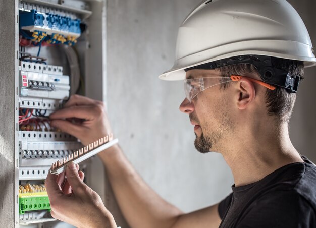 Mężczyzna, elektryk pracujący w tablicy rozdzielczej z bezpiecznikami. Instalacja i podłączenie sprzętu elektrycznego.